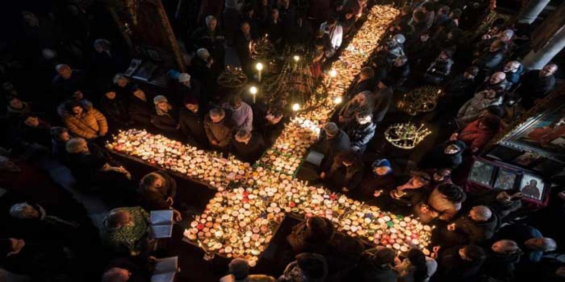 People surrounding cross made of candles